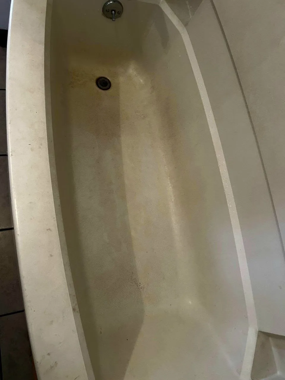 A bathtub with brown stains along the bottom, before cleaning