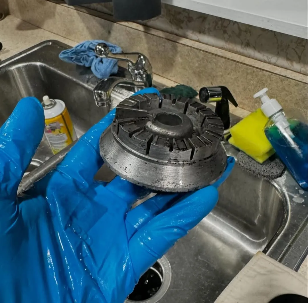 A gloved hand holding a burner cap that is cleaner, after scrubbing