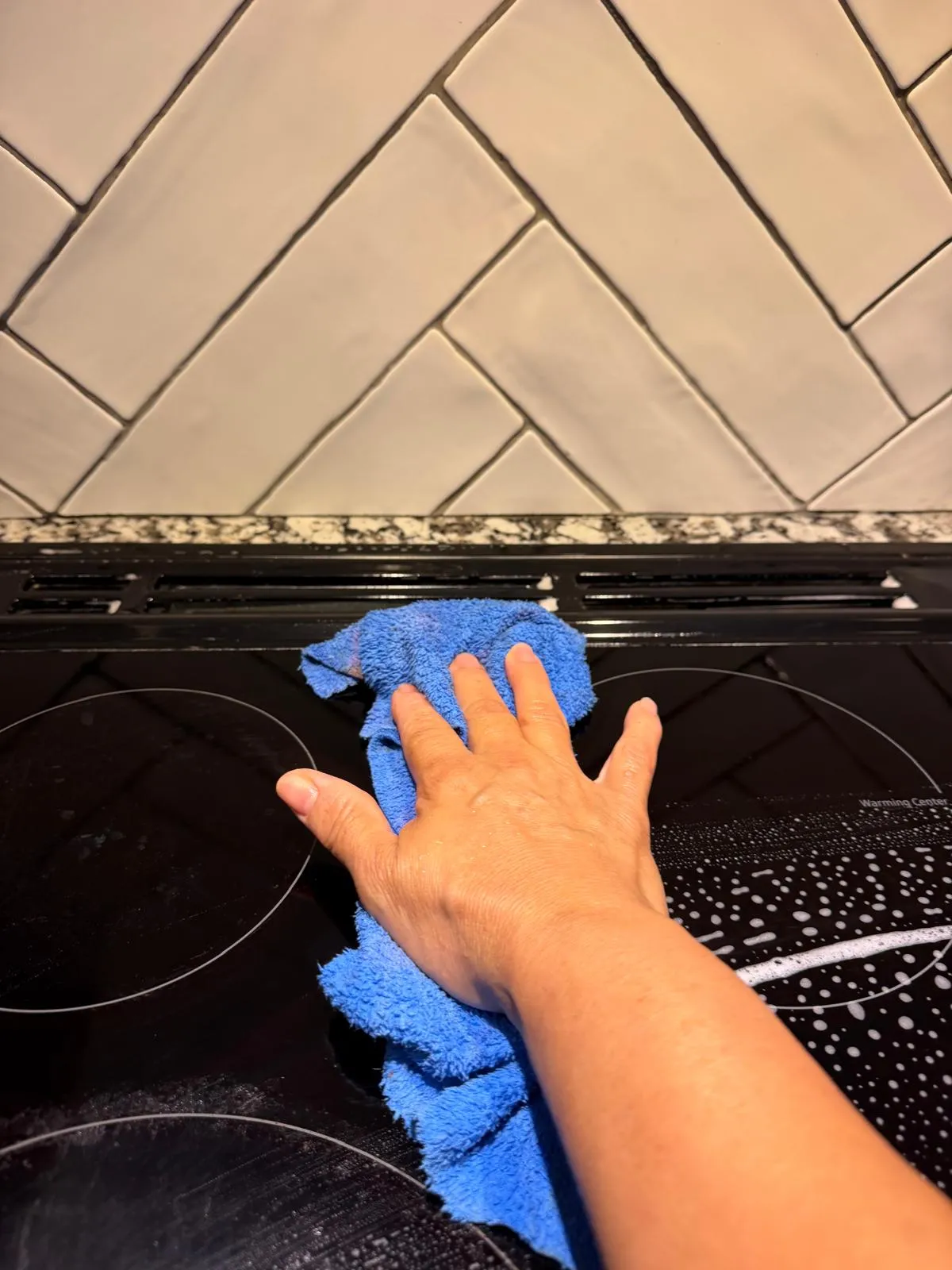 A hand wiping a black cooktop with a blue microfiber cloth