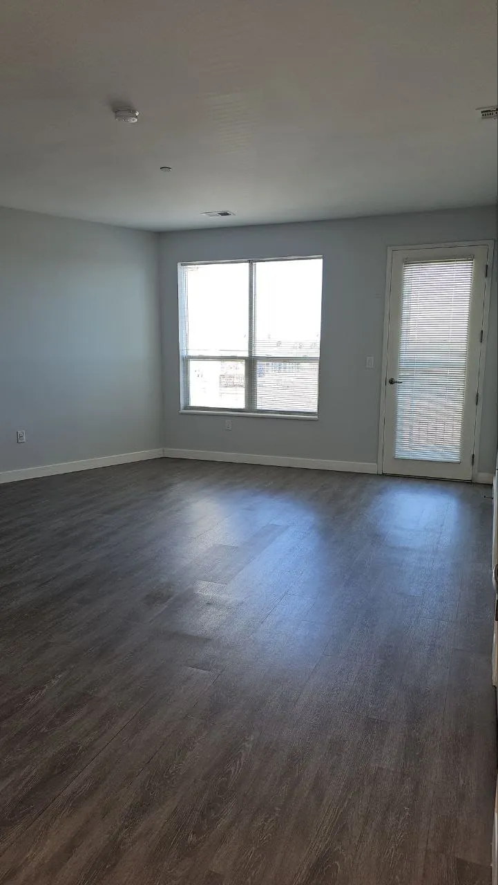 An empty living room with clean wood-look floors and two windows