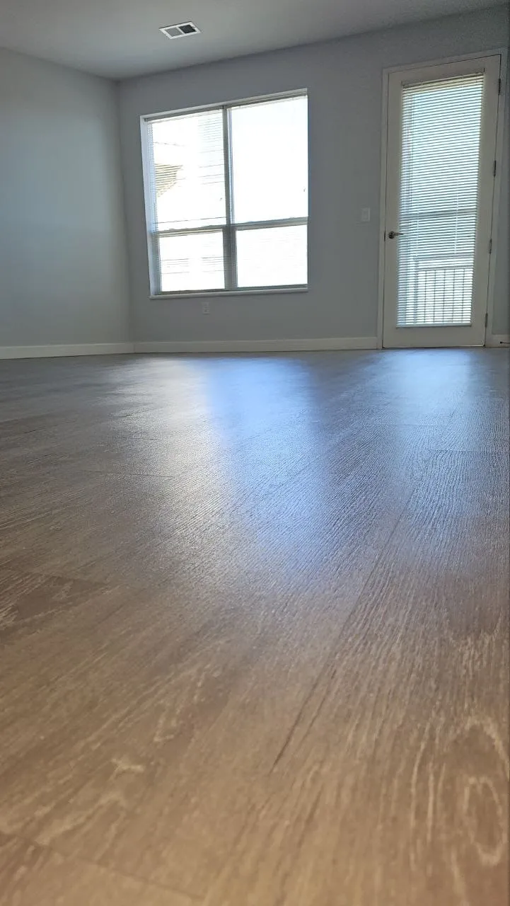An empty room with clean wood-look floors and large windows