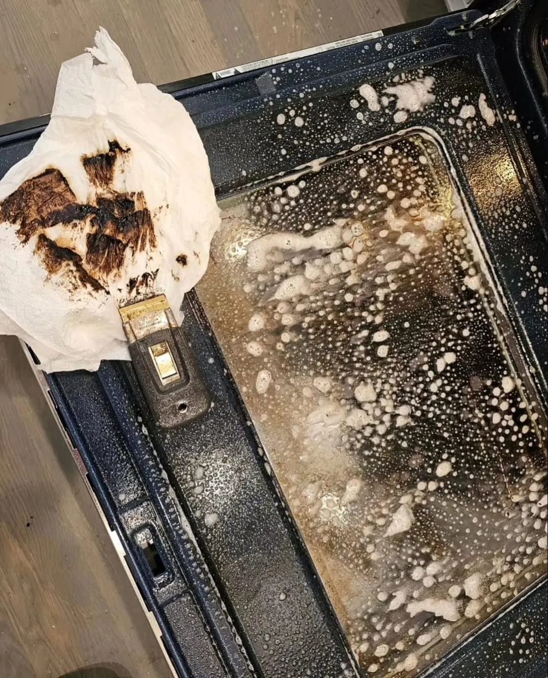 Foam and a paper towel on the glass of a dirty oven door